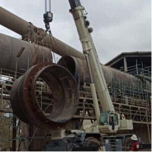 Rotary kiln shell segment lifted by crane during kiln shell replacement process. Deformations detected by hot kiln alignment service.
